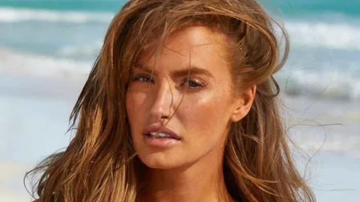 Haley Kalil poses in front of the ocean with her red hair down.